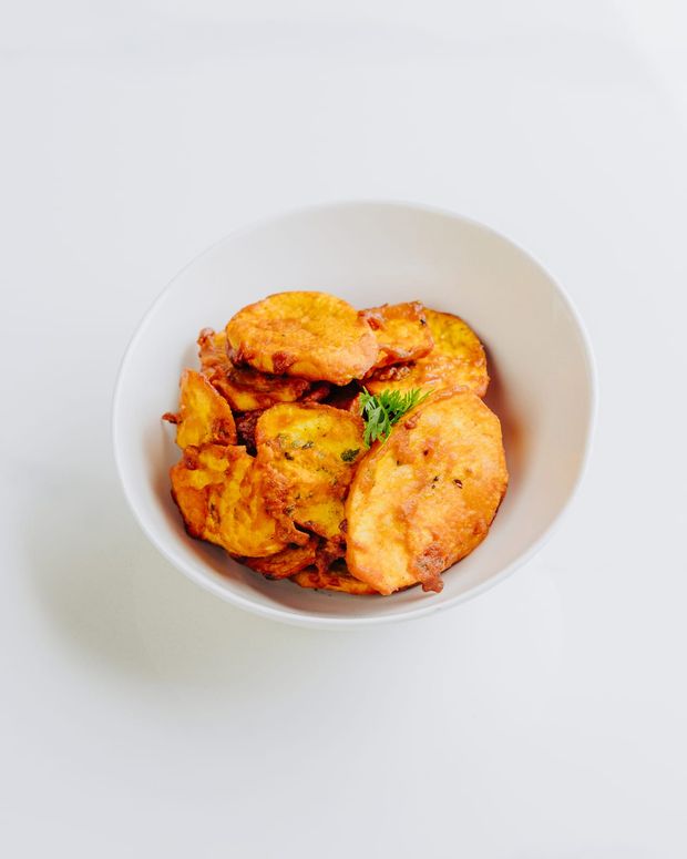 A white bowl of crisp battered potato bhajia topped with a sprig of fresh coriander
