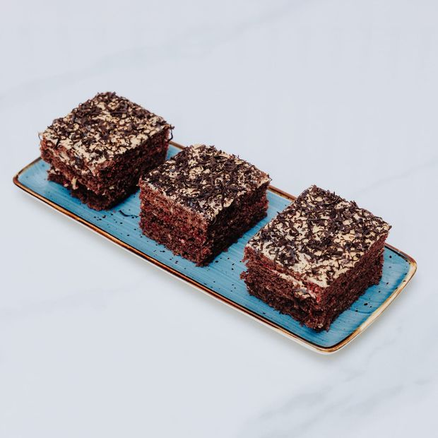 Three squares of black forest cake layered with cream and cherry, topped with chocolate shavings