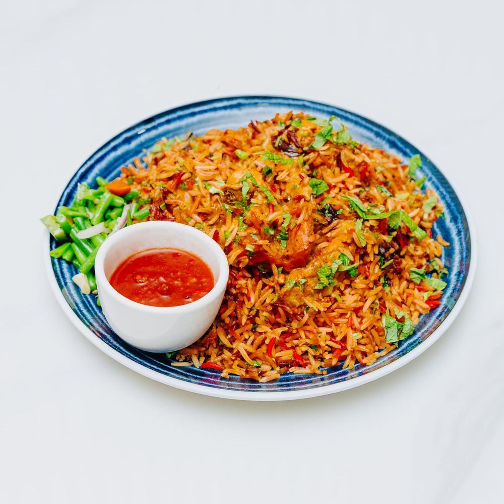 A plate heaped with spiced biryani rice studded with chicken, chillies, sultanas and fresh herbs