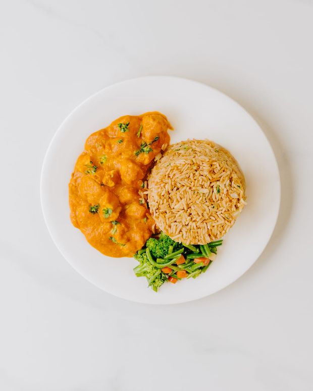 Creamy butter chicken with a mould of spiced rice, broccoli and carrots on a white plate