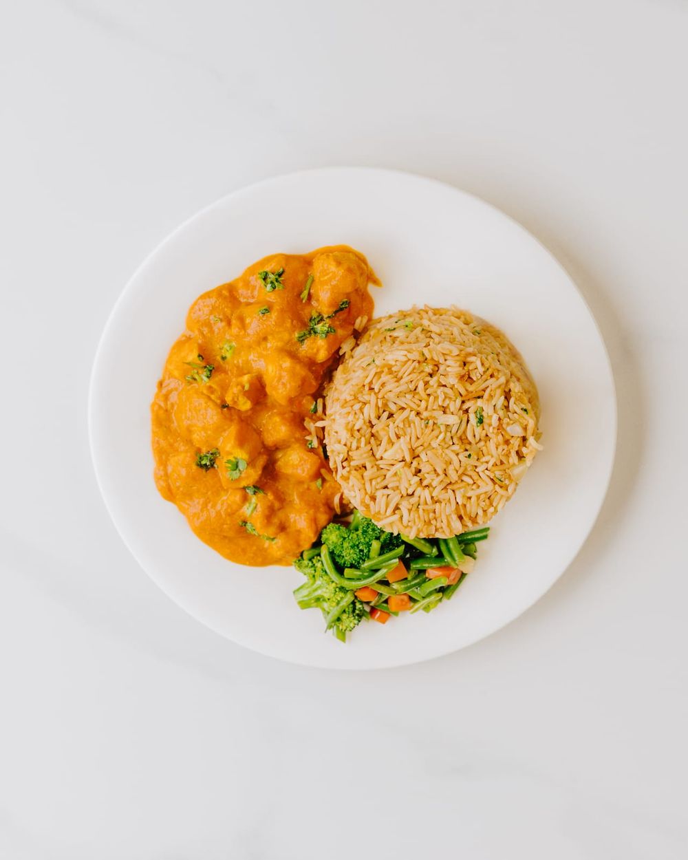 Creamy butter chicken with a mould of spiced rice, broccoli and carrots on a white plate