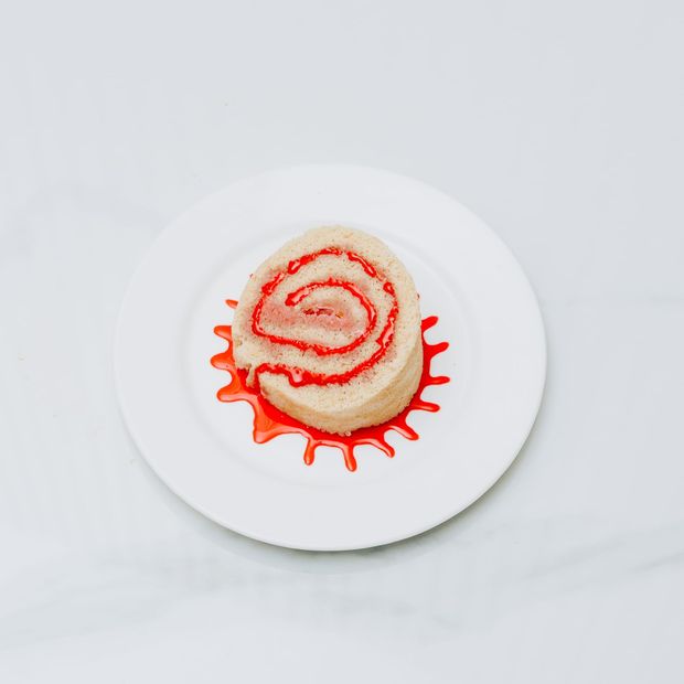 A slice of jam-filled sponge roll in a pool of strawberry sauce