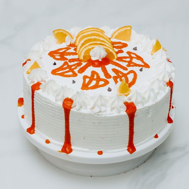 A whole cream-frosted cake with piped rosettes, orange sauce and chocolate chips