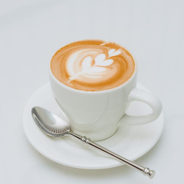A cappuccino with rosetta latte art in a white cup and saucer