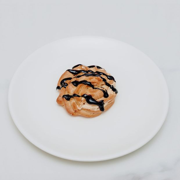 A cream-filled choux bun with a dark chocolate zigzag on a white plate