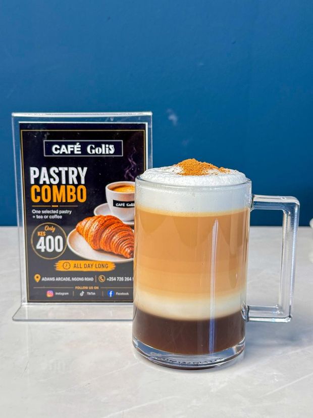 A glass tankard of layered coffee with a thick foam cap dusted with cocoa