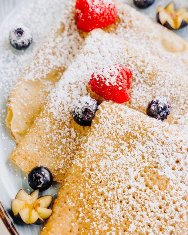 A close crop of a crêpe dusted with icing sugar, with raspberries and blueberries