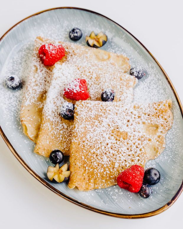 Three folded crêpes dusted with icing sugar and topped with raspberries and blueberries