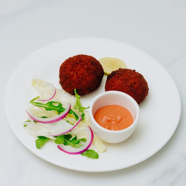 Two deep-fried crumbed patties with a lime wedge, a rocket and red onion salad, and a ramekin of pink sauce