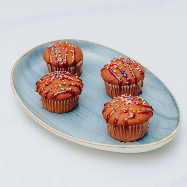 Four cupcakes drizzled with red syrup and covered in rainbow sprinkles, on a blue oval platter