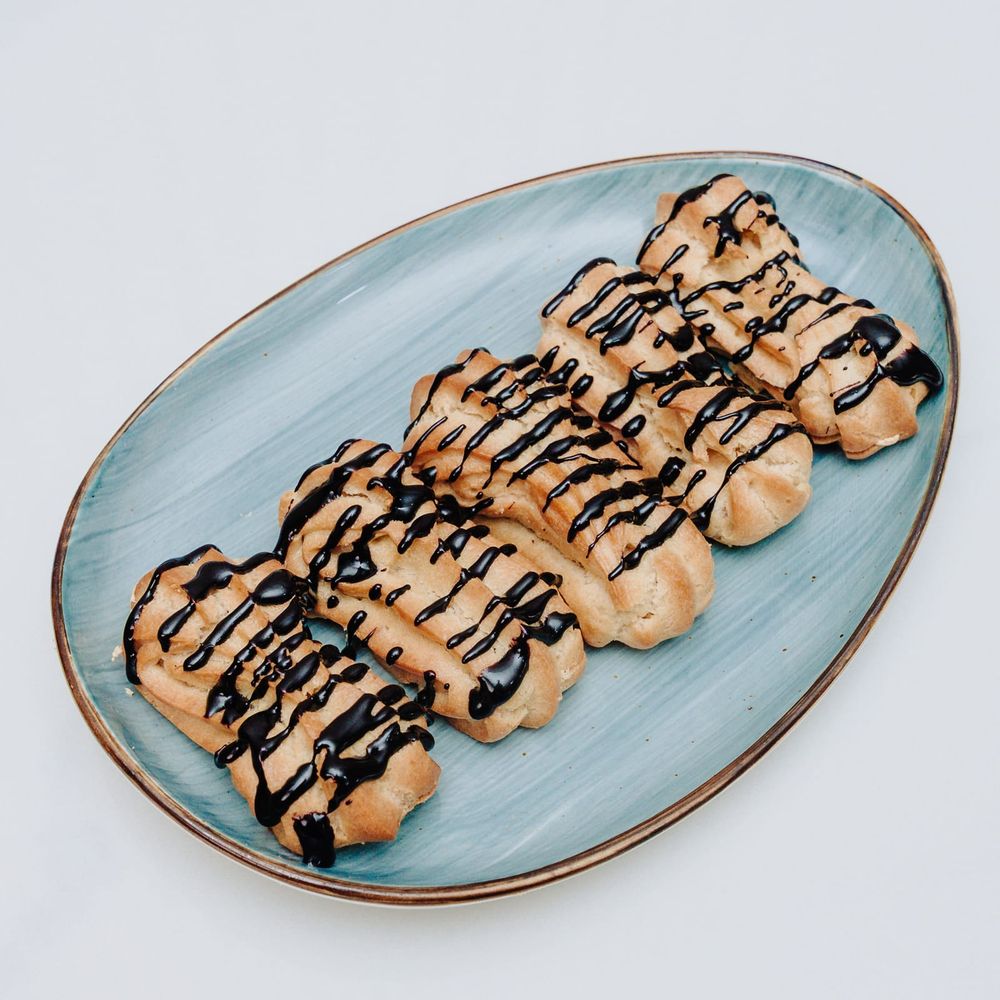 Five chocolate-glazed éclairs lined up on a blue-glazed platter