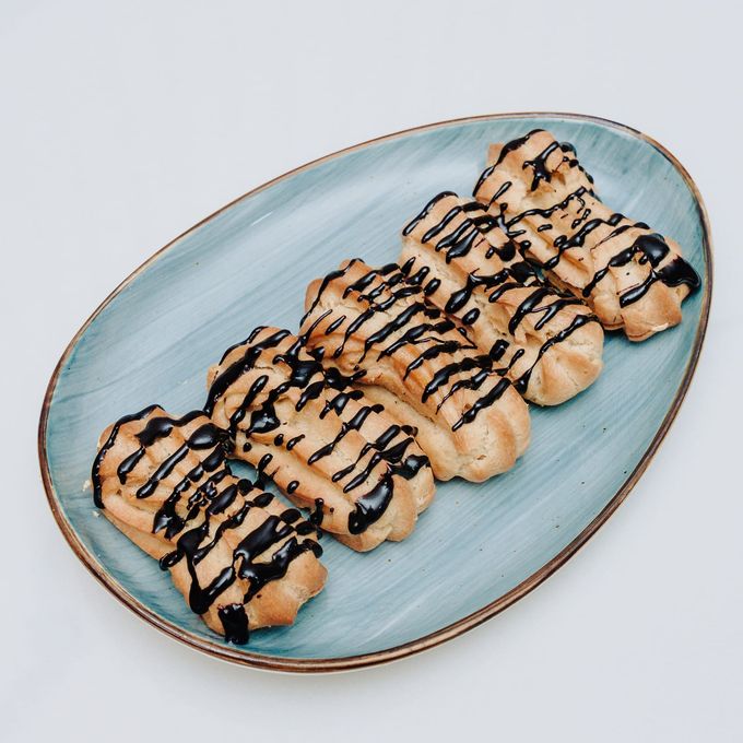 Five chocolate-glazed éclairs lined up on a blue-glazed platter