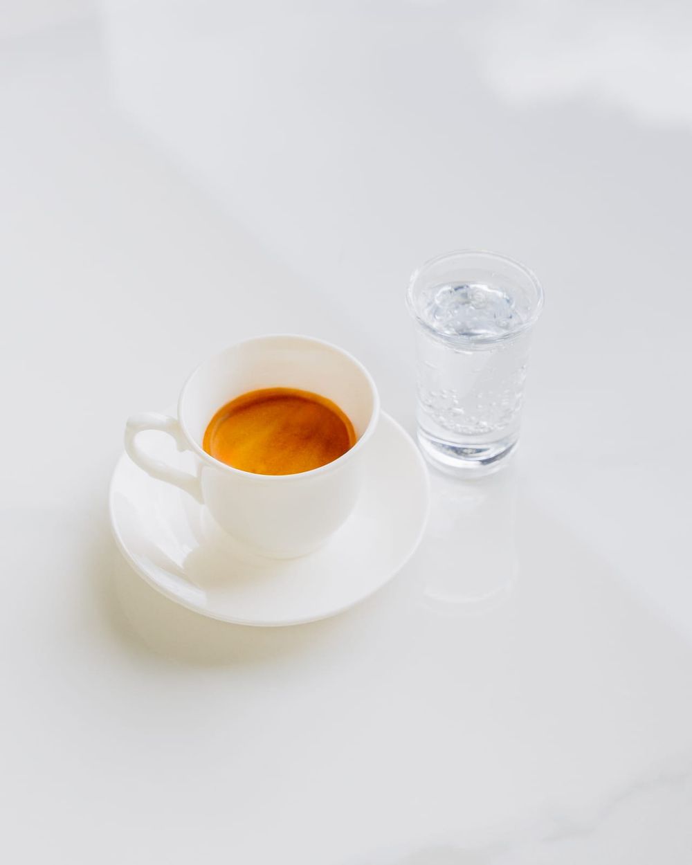 A single espresso with a hazelnut crema in a white cup, served with a small glass of water