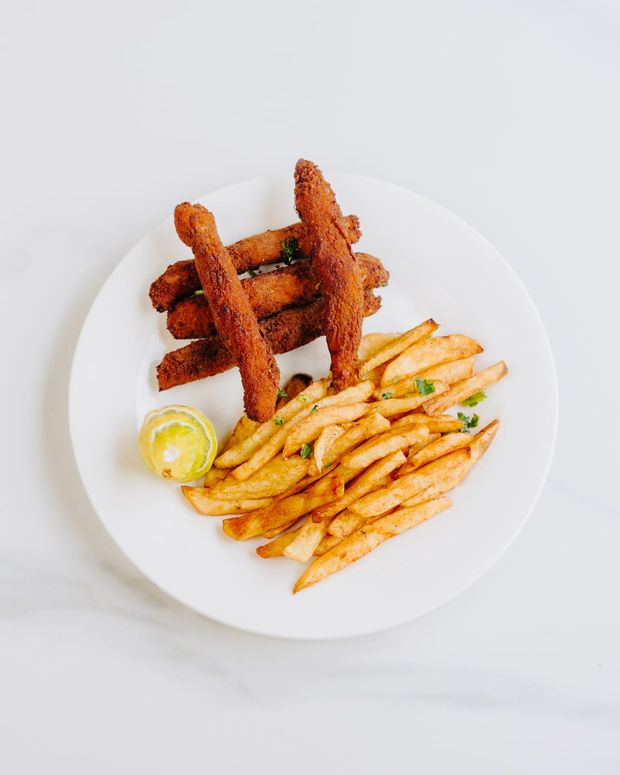 Golden breadcrumbed strips stacked over seasoned fries with half a lemon