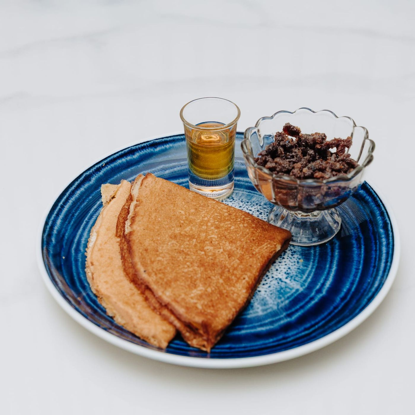 Two folded Somali flatbreads on a deep blue plate, beside a glass dish of crumbled dried camel meat and a small glass of ghee