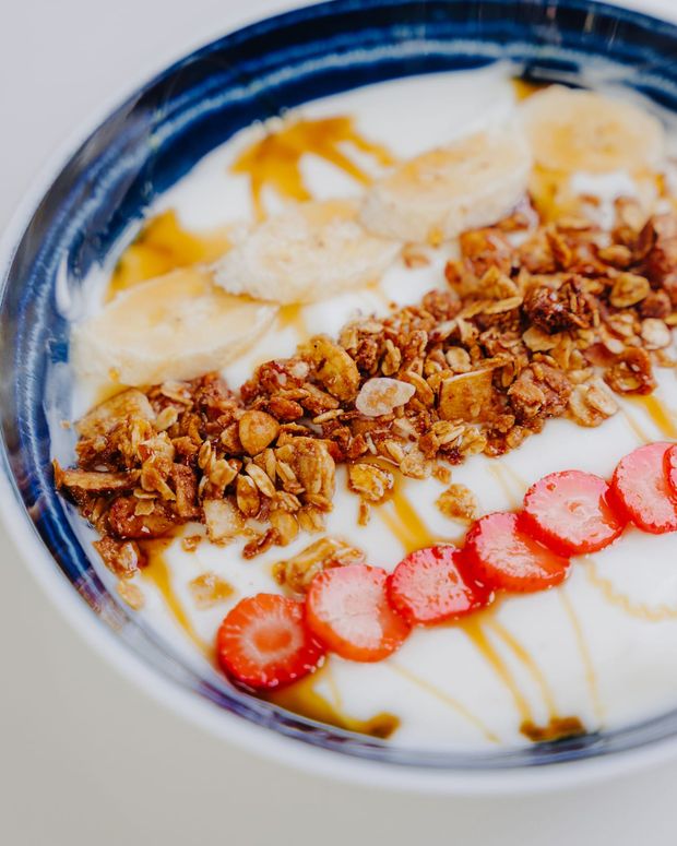 A close crop of yoghurt with a band of granola clusters, banana coins and halved strawberries