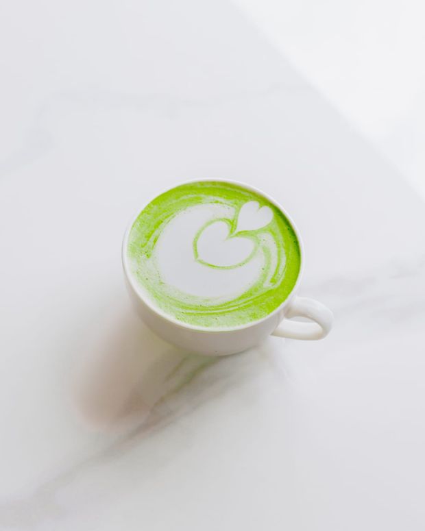 A matcha latte in a white cup, a white heart poured into vivid green, on pale marble