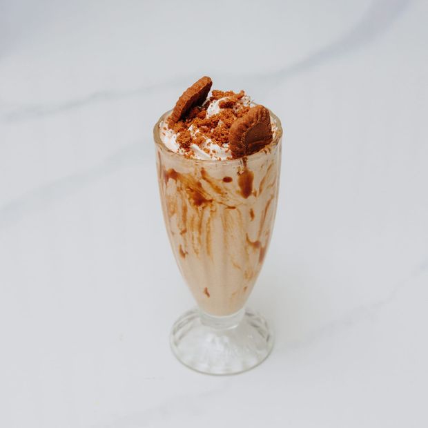 A tall caramel milkshake with whipped cream, biscuit pieces and crumb topping