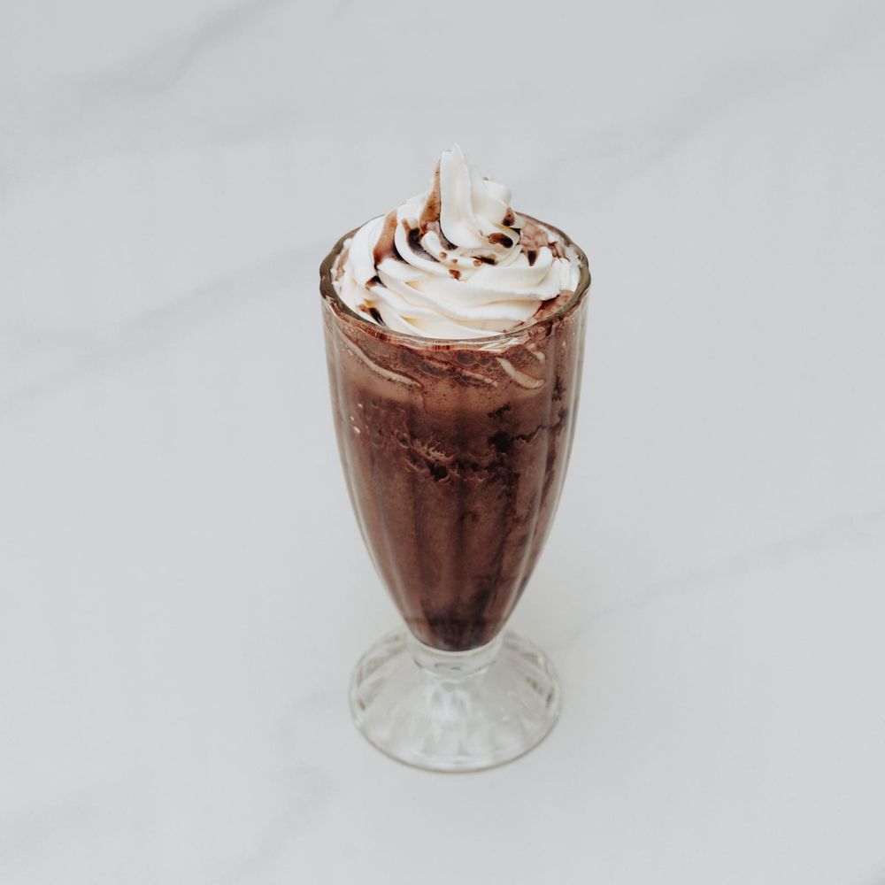 A tall chocolate milkshake with a swirl of whipped cream and chocolate drizzle