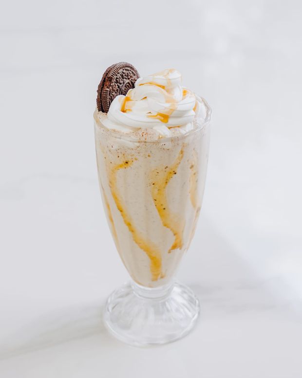 A tall milkshake with cookie pieces, caramel ribbons down the glass and a whipped cream crown