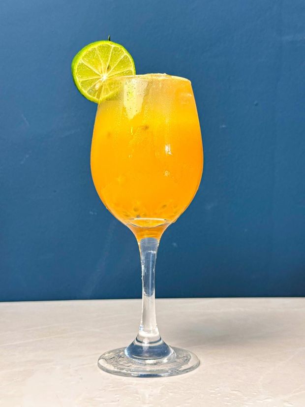 A stemmed glass of cloudy passion fruit mocktail with ice and a lime wheel on the rim