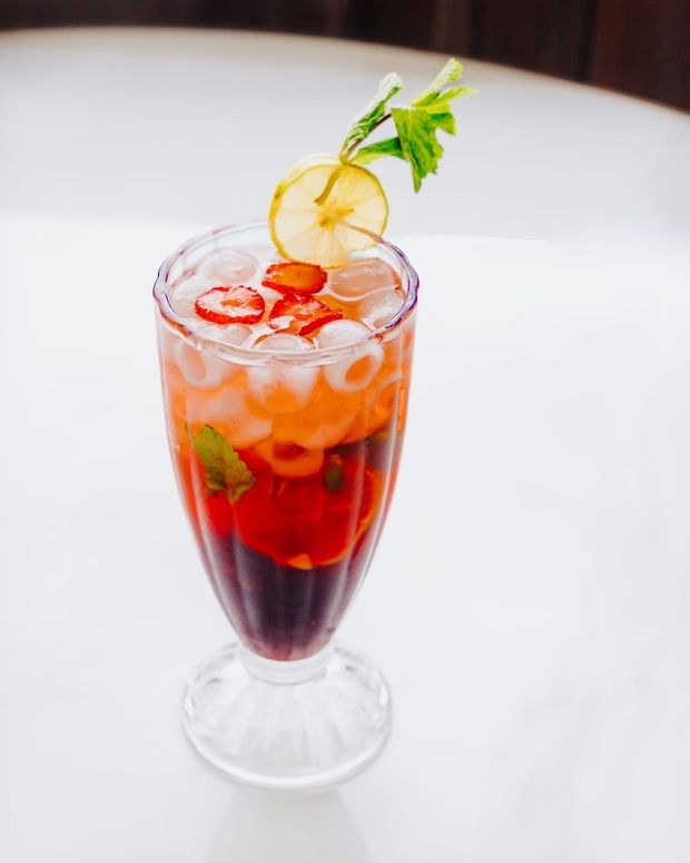 A tall layered red mocktail with sliced strawberries, mint and a dried lemon wheel