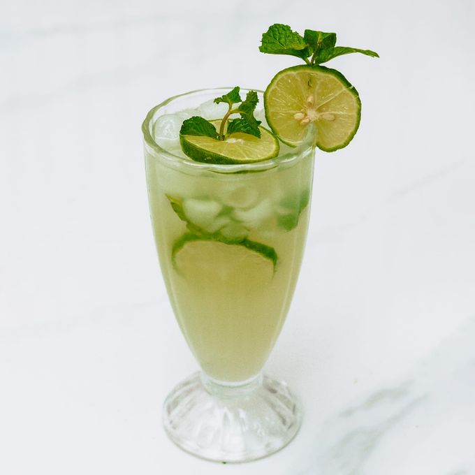 A tall footed glass of pale green mojito mocktail with lime wheels, ice and a sprig of mint