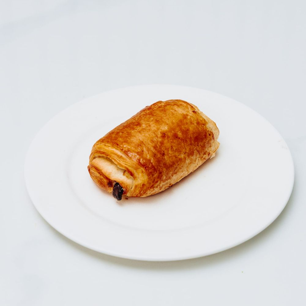 A golden, glossy pain au chocolat with dark chocolate visible at the end