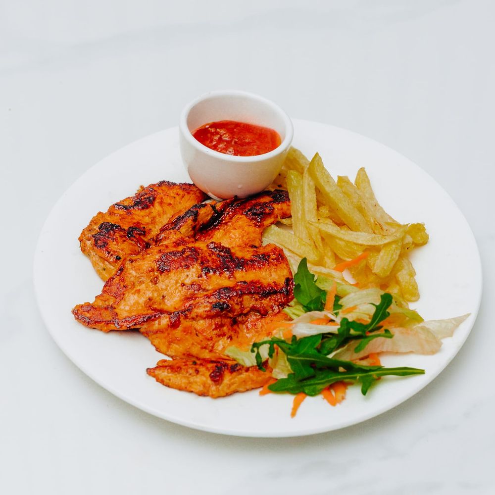 Charred peri-peri grilled chicken fillets with thin-cut chips, a crisp side salad and a ramekin of red sauce