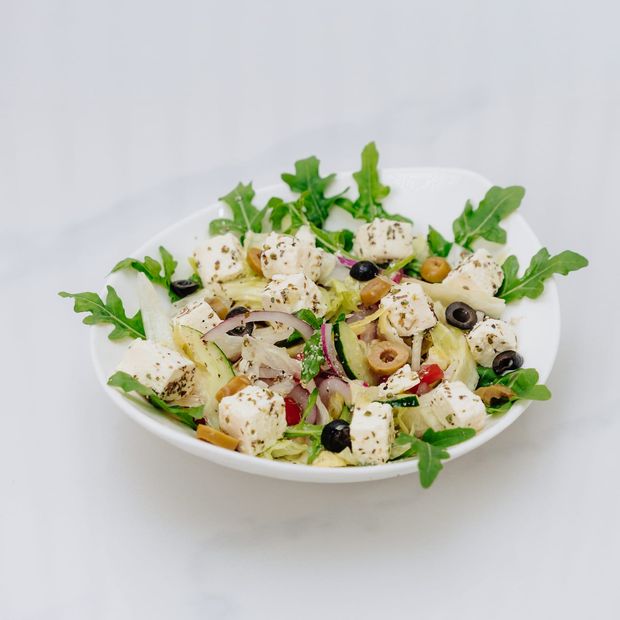 A salad of cubed feta, rocket, cucumber, red onion and olives in a white bowl