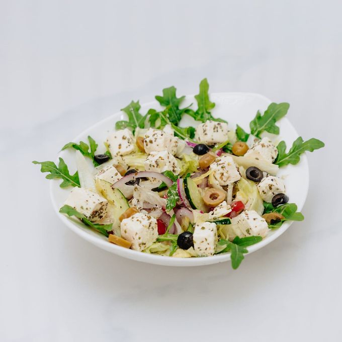 A salad of cubed feta, rocket, cucumber, red onion and olives in a white bowl