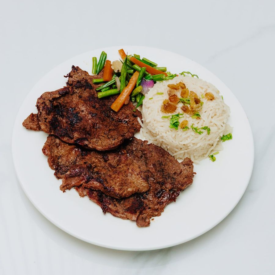 Two pan-seared steaks with green beans, carrot batons and a mould of rice on a white plate
