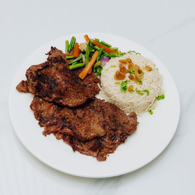 Two pan-seared steaks with green beans, carrot batons and a mould of rice on a white plate