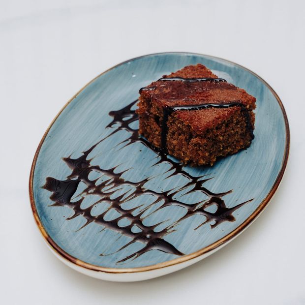 A square of sticky date cake in toffee sauce on a blue-glazed oval plate