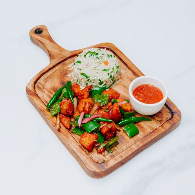 Stir-fried meat with capsicum, green chillies and red onion on a wooden board with herbed rice