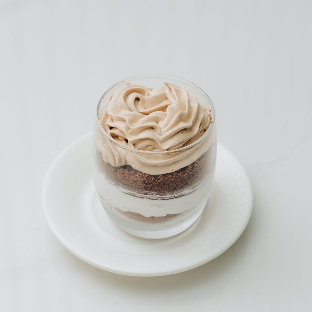 A layered tiramisu in a short glass with cocoa sponge, cream and piped coffee mousse